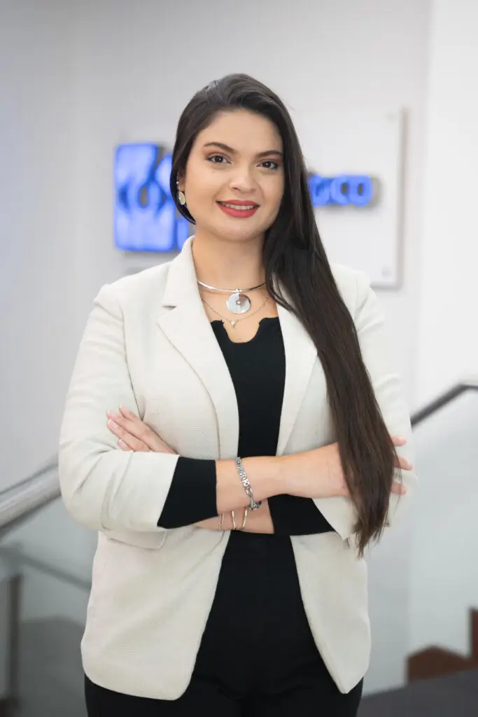 A smiling young woman with long dark hair and crossed arms wearing a blazer.