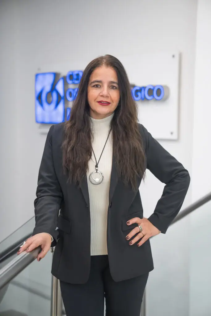A woman with long dark hair in a black blazer stands smiling.